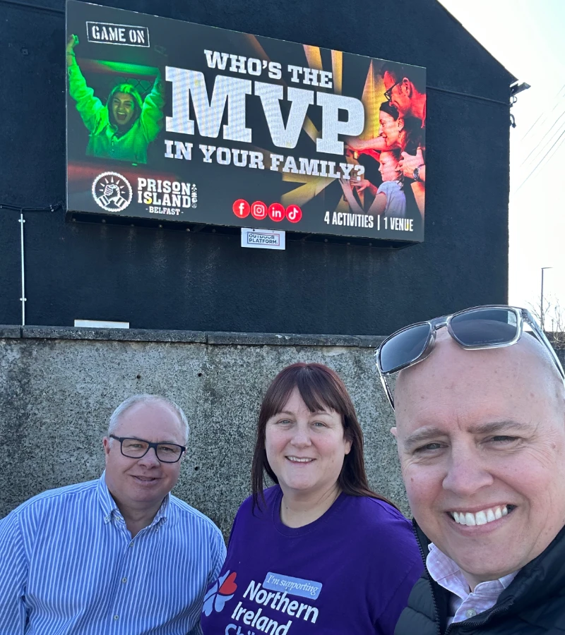The team with a Prison Island advert DOOH on display behind them in Ballymena